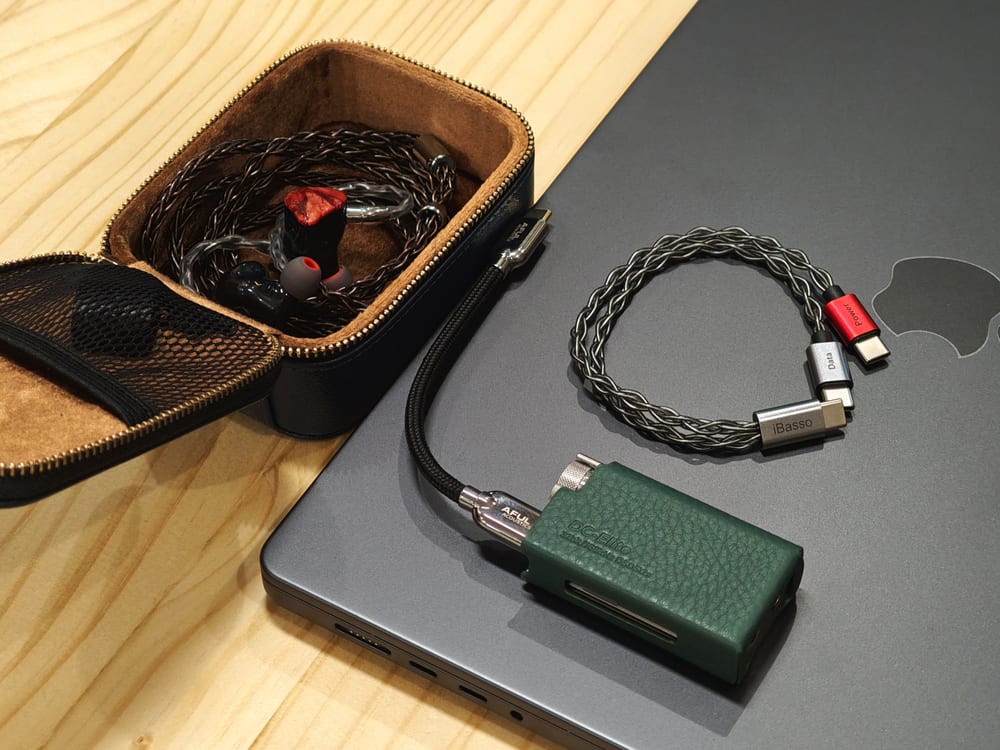 An AFUL in-ear monitor in its leather case beside an iBasso DC-Elite DAC/amp and a braided upgrade cable.